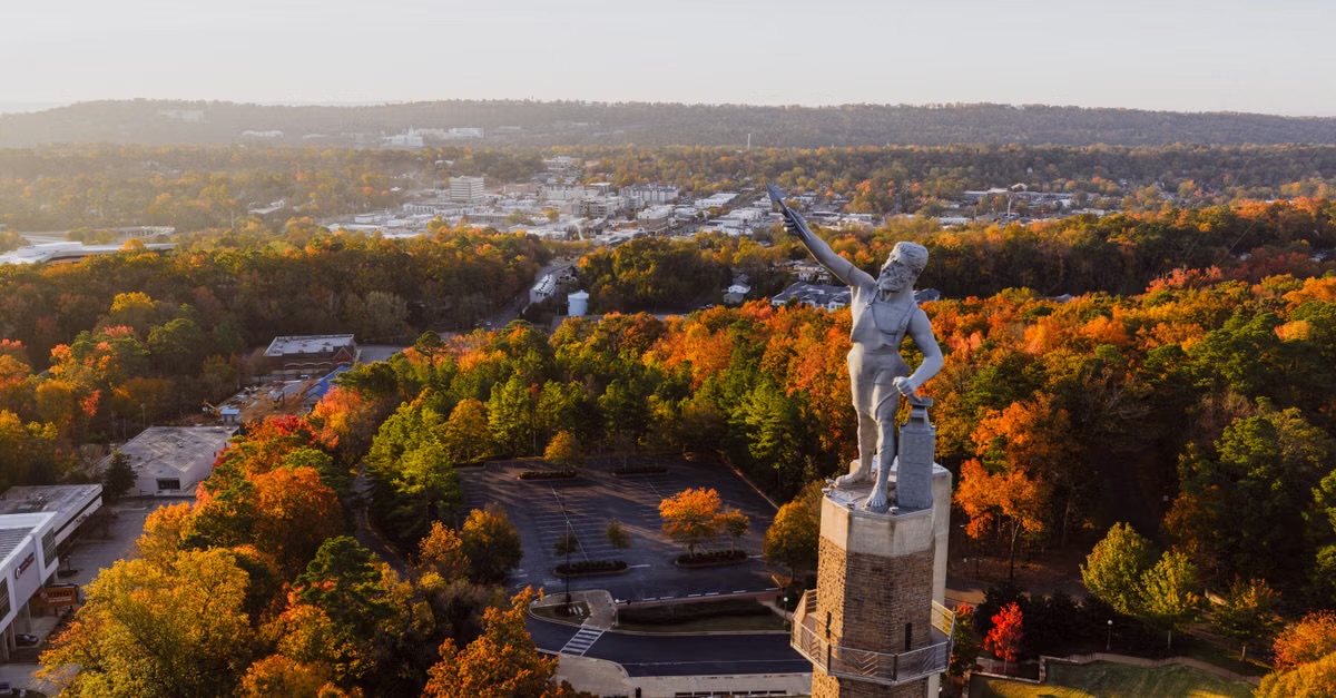 Aerial view of a hilltop statue above autumn treetops and a city below